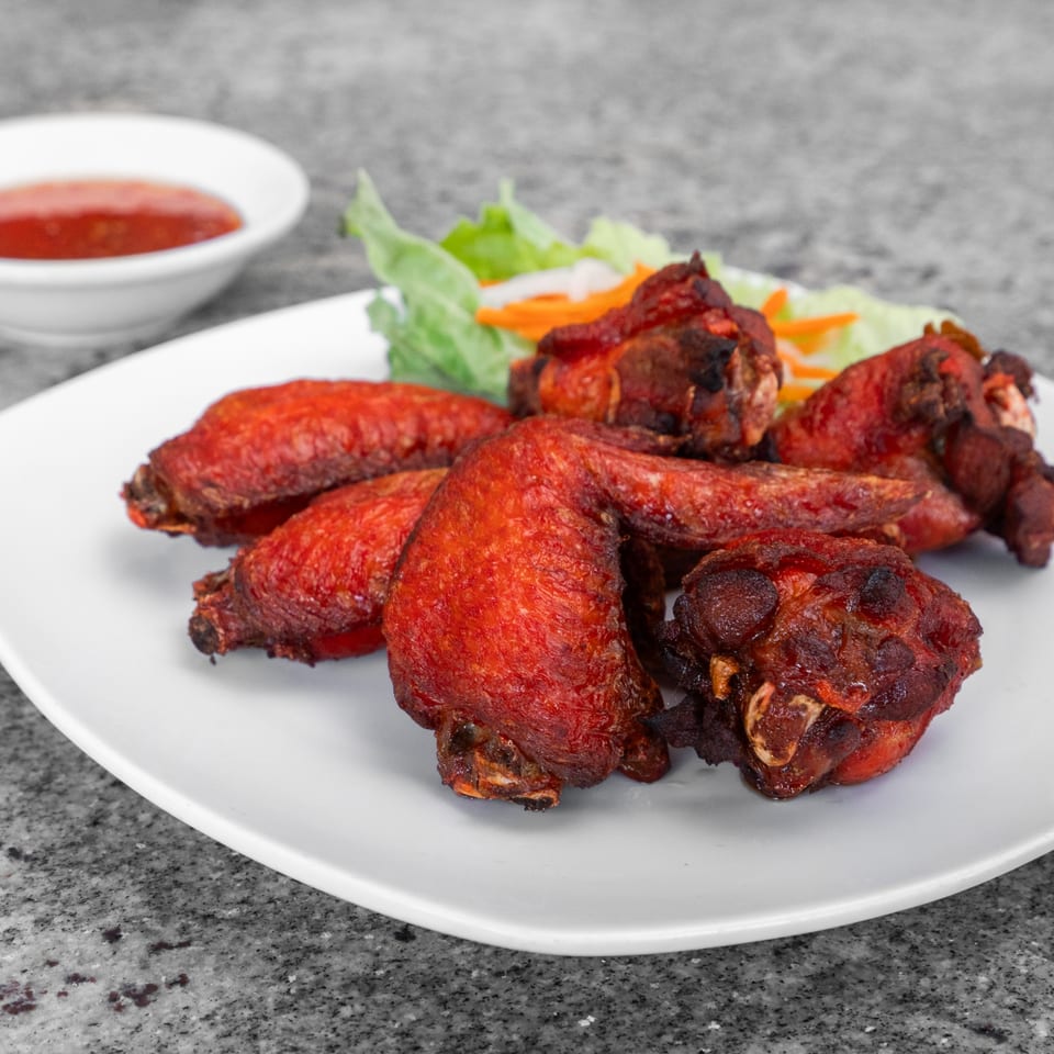 Crispy, red-glazed Vietnamese chicken wings with a side of fresh lettuce and pickled carrots.