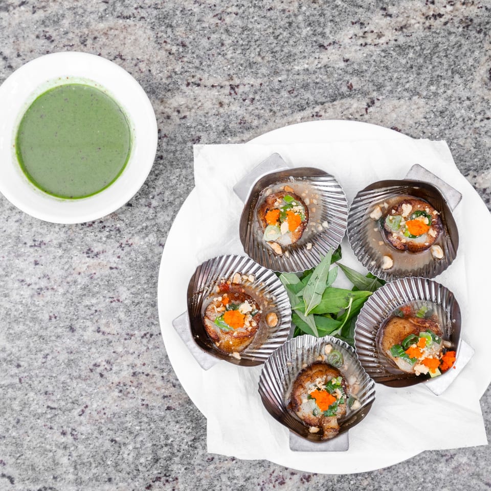 Vo An Vietnamese scallops in shells with green sauce, nuts, and herbs on a white plate.