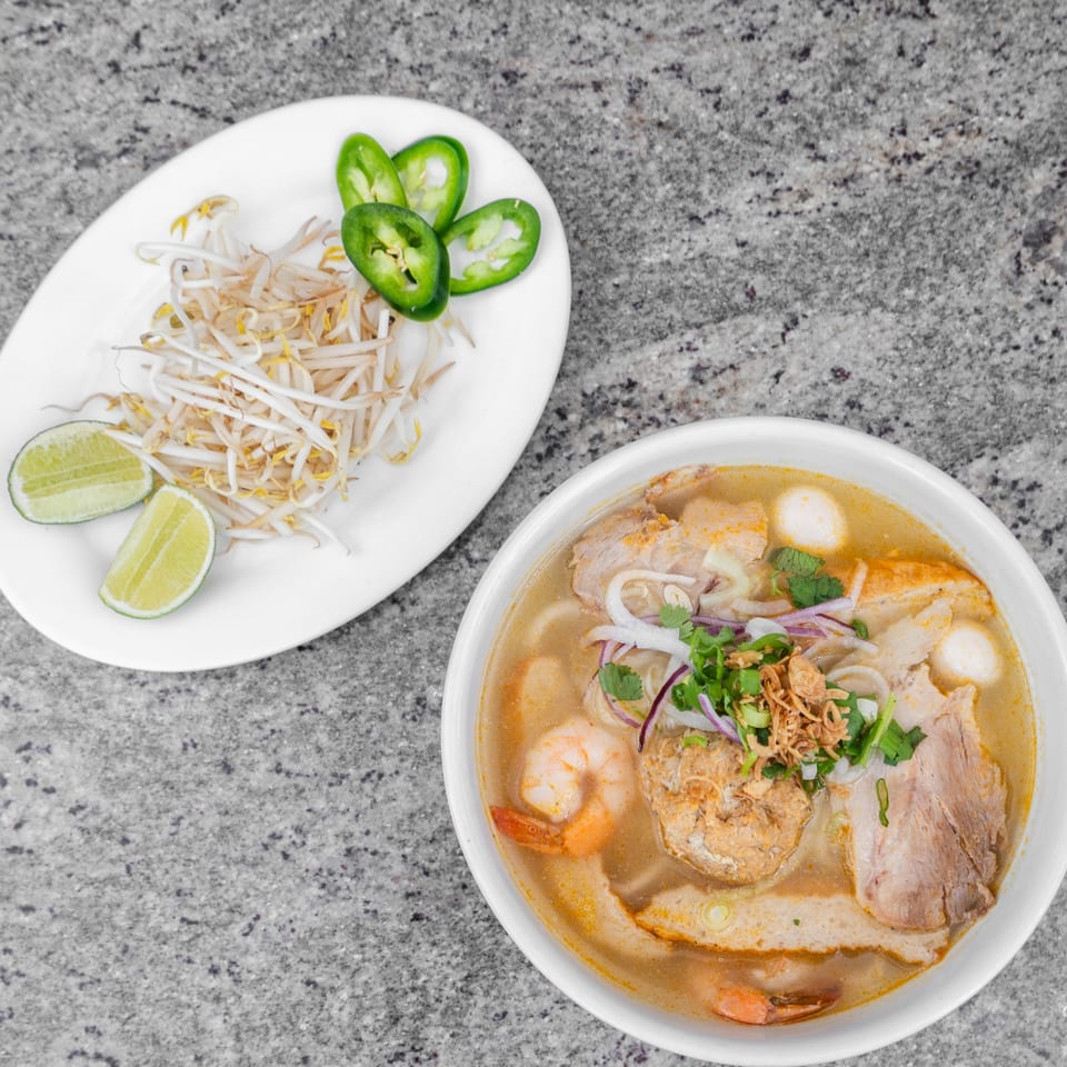 Overhead view of a Vietnamese noodle soup with shrimp, pork, and meatballs, served with bean sprouts and lime.