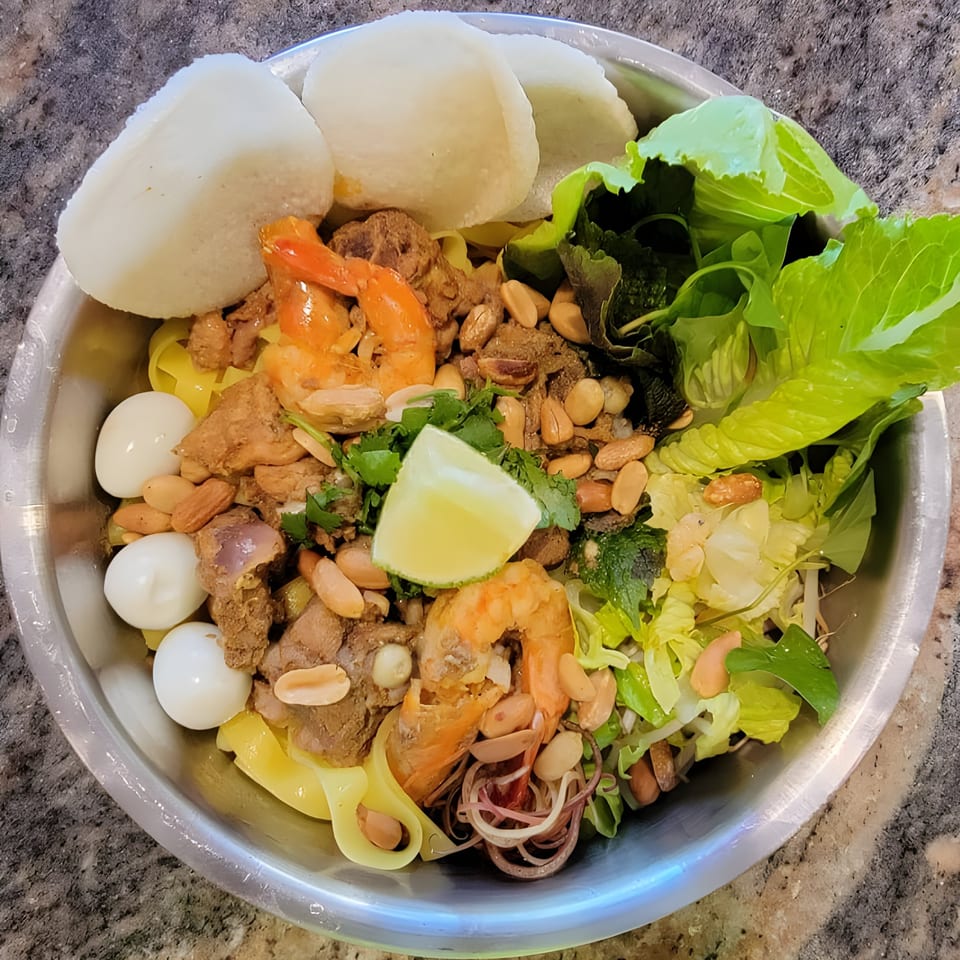 A vibrant Vietnamese dish with shrimp, meat, quail eggs, peanuts, and fresh greens in a metal bowl.